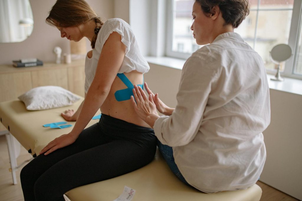 Chiropractor applying kinesiology tape to a woman's rib in a therapy session.