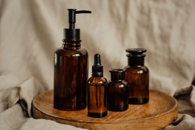 A collection of brown glass cosmetic bottles with a pump and pipette on a rustic wooden tray.