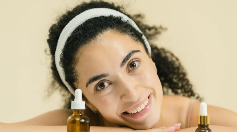 Woman with curly hair smiling, showcasing skincare products, indoors.